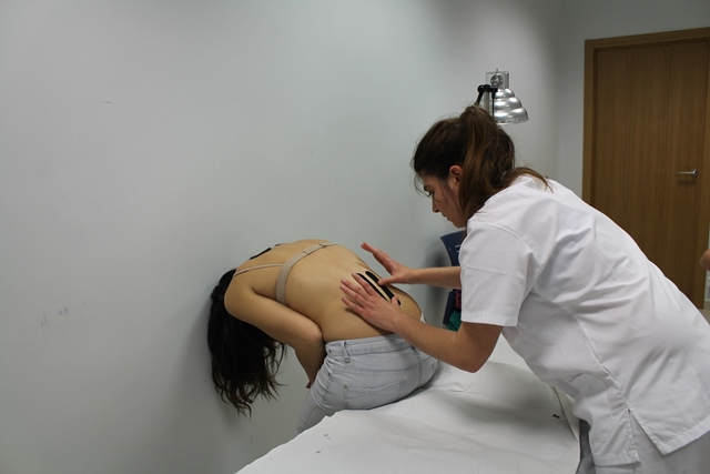 Una estudiante de fisioterapia coloca las tiras de kinesiotape a una costalera en la zona lumbar.